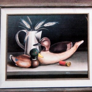 Op de afbeelding: Een ingelijst schilderij van een stilleven met twee houten eendenlokvogels, een kan en een patroonhuls. Het schilderij is getiteld "Tolé'n Afield" door Bob Embry.