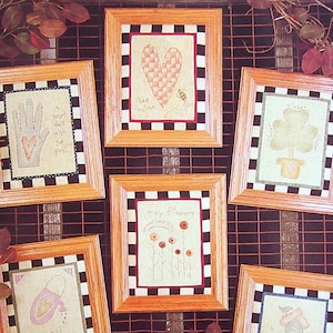 May include: A collection of 12 cross-stitch patterns for each month of the year. The patterns are framed in wood with black and white checkered borders. The patterns include a heart, a hand, a clover, flowers, a watering can, and a birdhouse.