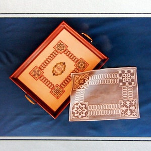 Puede incluir: Un primer plano de una bandeja de té de estilo vintage con un delicado diseño bordado. La bandeja es de madera y tiene un acabado marrón. El bordado es en tonos de blanco y crema. El texto "Tea Time Traditions" está impreso en la página. El texto "From the Victorian Patternworks Series" y "Featuring Sampler Threads from The Gentle Art" también está impreso en la página.