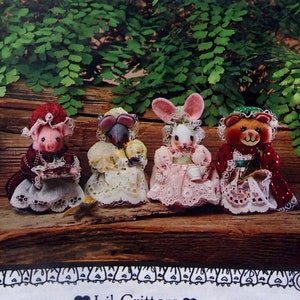 May include: A package featuring four Lil' Critters dolls: a pig, a bird, a bunny, and a bear, each dressed in detailed outfits. The dolls are set against a backdrop of greenery and wood. The package includes text that reads "Lov'n Stuff!" and "Creative Soft Designs by Karen & Barb."