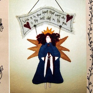 May include: A folk art style image featuring a felt angel holding a banner that reads "Write it in your heart that every day is the best day in the year." The angel has a blue dress, brown wings, and a gold crown. The image is framed with whimsical drawings.