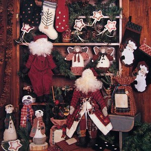 May include: A Christmas-themed image featuring a cupboard filled with handmade holiday decorations. The cupboard is adorned with stockings, stars, angels, and Santa Claus figures. The text "The Christmas Cupboard" is displayed at the top, with the brand name "thimbleberries, inc." at the bottom.