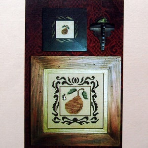 May include: A framed cross-stitch design featuring a pear with a leaf, set against a light background. The design is surrounded by a decorative border. The text "PEARS" and "OLDE WORLD INSPIRATIONS" are also visible.