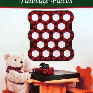 Peut inclure: Une couverture de livre représentant un ours en peluche blanc assis à une table en bois avec une courtepointe rouge et blanche accrochée au mur. Le titre du livre est "Yuletide Pieces" et l'auteur est "Tess Herlan & Deb Fenwick".