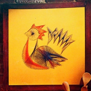 May include: A framed string art piece depicting a rooster in red, orange, and black thread on a yellow background. The frame is brown wood. The image is part of a book titled "The Royal-Craft Library by Cunningham 7136".