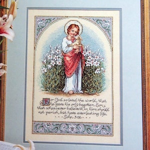Könnte beinhalten: Eine gerahmte Kreuzstichstickerei, die ein Kind mit einem Lamm inmitten weißer Lilien darstellt. Der Text lautet: For God so loved the world, that he gave his only begotten Son, that whosoever believeth in him should not perish, but have everlasting life. John 3:16.
