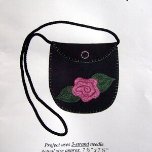 May include: A black felt bag with a pink rose and green leaves embroidered on the front. The bag has a strap and is labeled "Cabbage Rose" for punchneedle embroidery. The project uses a 3-strand needle and measures 7 1/2 inches by 7 1/2 inches.