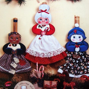 May include: A Christmas craft book titled "Button Button" by Cheryl Sims. The cover features three handmade ornaments: a black and white checkered doll, a red and white Santa doll, and a blue and white snowman doll. The ornaments are decorated with buttons and other embellishments.
