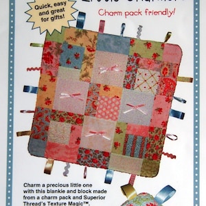Könnte beinhalten: Eine Patchwork-Babydecke mit bunten Bändern und einer kleinen, passenden, gesteppten Kugel. Die Decke ist aus einem Charm Pack gefertigt und hat eine weiche, plüschige Rückseite. Der Text "Little Charmers Charm pack friendly!" ist auf der Seite gedruckt.