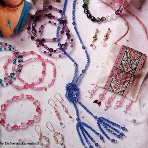 May include: A collection of crystal jewelry, including bracelets, necklaces, and earrings, displayed on a white surface. The image features a woman and the text "Crystals with Stretchy Cord". Various colors of crystals are visible.