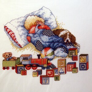 Könnte beinhalten: Gezähltes Kreuzstich-Muster für ein Kind, das auf einem Kissen mit einem Teddybär und einem Spielzeugzug schläft. Das Muster trägt den Titel "Sleep Tight" und die Nummer ST1003. Die fertige Größe beträgt 8 Zoll mal 9 Zoll.