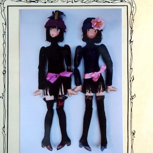 Op de afbeelding: Een vintage naaipatroon voor een 45,7 cm grote stoffen pop, getiteld "Magic Threads Flapper". Het patroon toont twee poppen gekleed in zwarte flapperjurken met roze sjerpen en zwarte kousen. Het patroon is auteursrechtelijk beschermd 1990 door Julie McCullough.