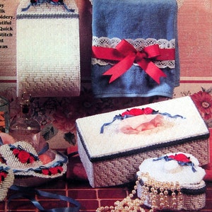 May include: A set of seven plastic canvas bath accessories with a floral theme. The set includes a towel rack, a toilet paper holder, a tissue box, a soap dish, a jewelry box, and two small baskets. The accessories are all white with red roses and blue ribbon accents. The text "Bath Ensemble" is printed on the image.