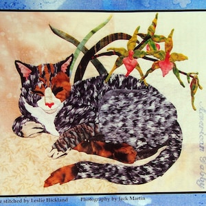 May include: A fabric quilt block featuring a sleeping American Tabby cat with orange, black, and white markings. The cat is surrounded by green leaves and red and yellow flowers. The text "My Cats Garden" and "American Tabby" are visible.