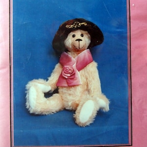 May include: A 14-inch fully jointed teddy bear wearing a black hat with a gold accent and a pink scarf with a rose. The bear is sitting on a blue background. The Teddy Tailor Presents "Honeysuckle" A 14 inch Fully Jointed Teddy and Hat The Teddy Tailor P.O. Box 234, Sutherlin, OR 97479 (503) 459-9517