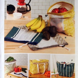 May include: McCall's pattern featuring various reusable shopping bags and produce storage solutions. Includes mesh bags, tote bags, and a zippered bag, alongside images of produce and a coffee maker. The pattern is designed and printed in the USA.