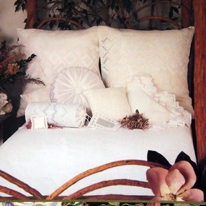 May include: A white bed with a wooden headboard and a white crocheted bedspread. There are several white crocheted pillows on the bed, including a round pillow with a floral design.