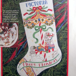 May include: A cross-stitch Christmas stocking kit featuring a carousel design with the name "Victoria" at the top. The stocking is white with a red border and includes the text "Merry Christmas". Finished size is approximately 16 inches (40cm) long.