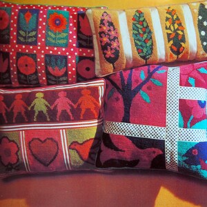 May include: A collection of decorative throw pillows with colorful, embroidered designs. Pillows feature floral, geometric, and folk art patterns in red, pink, green, and orange. The pillows are arranged on a yellow surface.