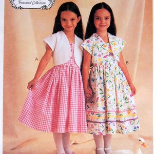 May include: McCall's sewing pattern showing two girls in dresses. One is pink gingham, the other floral. The pattern includes a white bolero jacket. Text includes "Ruffles and Lace Treasured Collection" and "Size CF (4,5,6)". Measurements are in inches.