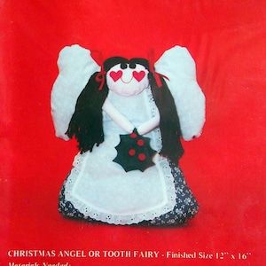 May include: A Christmas angel or tooth fairy doll pattern from That Patchwork Place. The pattern includes instructions for making a 12-inch by 16-inch doll with white wings, a white dress, a blue and white apron, and black hair. The doll is holding a green holly sprig with red berries.