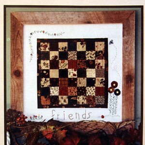 May include: A framed quilt pattern titled "Block Garden" by Mountain Patchwork. The quilt design features a checkerboard pattern in shades of brown, black, and cream. The word "friends" is stitched below the quilt. The image is decorated with leaves and floral accents.