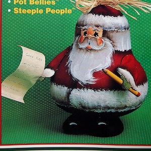 Puede incluir: Una figura de Papá Noel de papel maché con un traje rojo, barba blanca y una lista que dice "Good Kids". La imagen es de la serie "Holiday Happenings" y presenta el texto "Claus Clan".