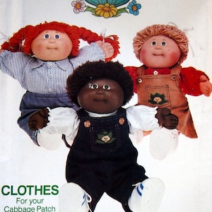 Op de afbeelding: Een vintage naaipatroon voor Cabbage Patch Kids kleding. Het patroon toont drie poppen die verschillende outfits dragen: een blauw-wit gestreept shirt, een bruine overalljurk en een denim overall outfit. Het patroon heeft de titel "Cabbage Patch Kids" en heeft het nummer 6508 erop gedrukt. De tekst "Clothes for your Cabbage Patch Kids!" is onder de poppen gedrukt.
