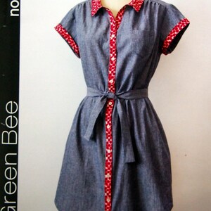 May include: A blue dress pattern labeled "Frances" with red and white patterned trim on the collar, cuffs, and button placket. The dress has a tie waist and is displayed on a mannequin. The pattern is from Green Bee.
