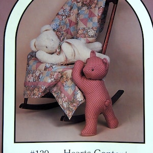 May include: A sewing pattern for a 20-inch lying bear and quilt. The pattern is titled "Hearts Content" and is from Great American Quilt Factory, Inc. The pattern shows a white bear lying on a rocking chair with a pink and white quilt. A pink bear is standing next to the rocking chair.