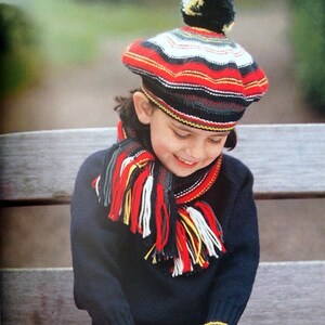 Peut inclure: Un enfant portant un pull noir, un béret rayé rouge, blanc et noir avec un pompon blanc et une écharpe rayée rouge, blanc, noir et jaune. L'enfant porte également des gants rayés rouge, blanc, noir et jaune. L'enfant est assis sur un banc en bois.