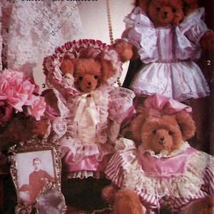 Op de afbeelding: Een Simplicity Crafts naaipatroon envelop 7597 door Faith Van Zanten met drie bruine teddyberen gekleed in roze en witte outfits met ruches en kanten randen, vergezeld door een klein ingelijst portret en een snoer van witte parels.