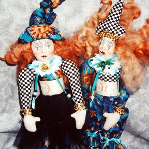 Könnte beinhalten: Zwei handgefertigte Puppen, die als Clowns verkleidet sind. Die Puppe links trägt einen blauen und goldenen Hut, ein schwarz-weiß kariertes Oberteil, einen schwarzen Rock und blaue Schuhe. Die Puppe rechts trägt einen schwarz-weiß kariertes Hut, ein blaues und goldenes Oberteil und blaue Schuhe.