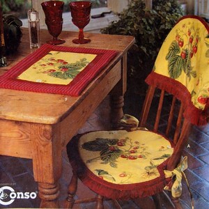 May include: A home decor pattern showing a wooden table with a red-trimmed placemat and two red goblets. A wooden chair with a yellow seat and backrest, decorated with a strawberry design, is also visible. The pattern includes chair covers, place mats, and a table runner.
