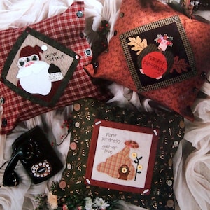 May include: A book titled "Pillow Talk Art to Heart" featuring three decorative pillows with embroidered designs. The pillows feature a Santa Claus, a turkey with the text "Harvest Blessings", and a bird with the text "Plant Kindness Gather Love".