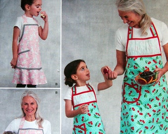 May include: Simplicity pattern 8815 features aprons in various styles. One apron has a pink background with white cat illustrations, while another is turquoise with red cherries. The pattern includes sizes S-L.