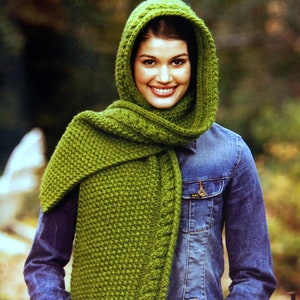 May include: A bright green hooded scarf featuring a textured knit pattern with a thick cable knit border along the edges. The scarf is draped over the shoulders and includes an integrated hood that frames the head, worn over a blue denim jacket.