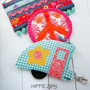 May include: Three colorful zippered pouches with a peace sign, a flower, and a camper van design. The pouches are made of fabric and have a zipper closure. The pouches are labeled "Hippie Zips".