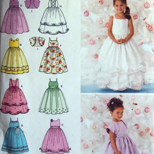 Op de afbeelding: Simplicity naaipatroon met verschillende meisjesjurken, waaronder een witte jurk met bloemaccenten en een lavendelkleurige jurk. Het patroon bevat verschillende jurkstijlen en maten 5, 6, 7 en 8.