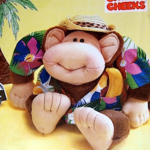 May include: A plush monkey toy wearing a straw hat and a colorful Hawaiian shirt. The monkey has a big smile and is holding a banana. The toy is part of the "Chubby Cheeks" line of crafts.