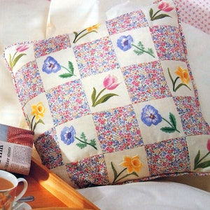 Peut inclure: Un oreiller blanc à motif à carreaux avec des fleurs brodées dans des tons de rose, jaune, bleu et vert. L'oreiller est posé sur une housse de couette blanche.