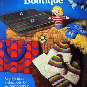 May include: A book cover with the title "The Needlework Boutique" by Annette Feldman. The cover features a variety of crocheted items, including a doll, a scarf, a hat, and mittens. The book promises 47 new boutique projects to make in less than 24 hours.