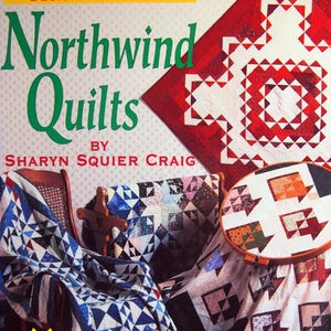 May include: A book cover titled Design Challenge: Northwind Quilts by Sharyn Squier Craig. The cover features a red and white quilt, a blue and white quilt draped over a chair, and a circular embroidery hoop displaying a quilt block pattern.