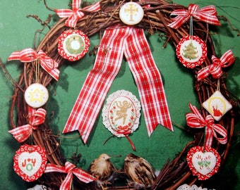 Könnte beinhalten: Ein Weihnachtskranz mit rot-weißem Gingham-Band und Perlenornamenten. Die Ornamente sind mit verschiedenen Weihnachtsthemen gestickt, darunter ein Stern, ein Baum, eine Glocke und ein Kranz. Der Kranz ist von zwei Vögeln und einem Korb mit rot-weißen Ornamenten umgeben.