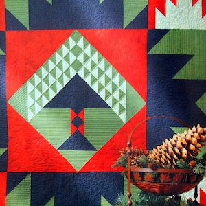 May include: A quilt with a geometric pattern in red, green, and blue. The quilt is hanging on a wall and a tiered stand with pine cones and greenery is in front of it.