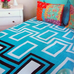 May include: A turquoise blue bed with a white and black geometric patterned quilt. The bed has a wooden headboard with a turquoise blue finish. The bed is decorated with colourful pillows.
