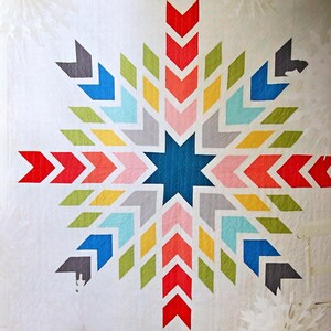 Peut inclure: Une courtepointe colorée avec un motif en étoile éclatante mettant en vedette une grande étoile bleue au centre. La courtepointe est composée de différentes nuances de rouge, orange, jaune, vert, bleu et rose.