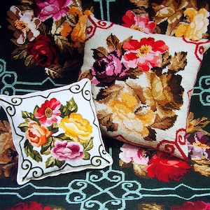 May include: Two square throw pillows with floral needlepoint designs. One pillow features a large arrangement of red, pink, and yellow roses on a cream background. The other pillow has a similar design with a white border and green swirls.