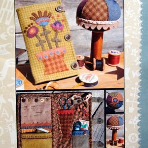 May include: A handmade needlebook and pincushion set. The needlebook features a floral design with button closures. The pincushion is a mushroom shape with a wooden base. The image also includes spools of thread and the text "Hatched and Patched".
