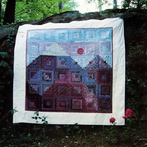 Op de afbeelding: Een quilt met een paarse berg scène, met een rode zon in de lucht. De quilt is gemaakt van vierkanten en rechthoeken in tinten paars, blauw en roze. De tekst "Purple Mountain Majesties" is onder de quilt gedrukt. Quilt van Patricia Litwiller Cooper, Middletoen, Illinois.
